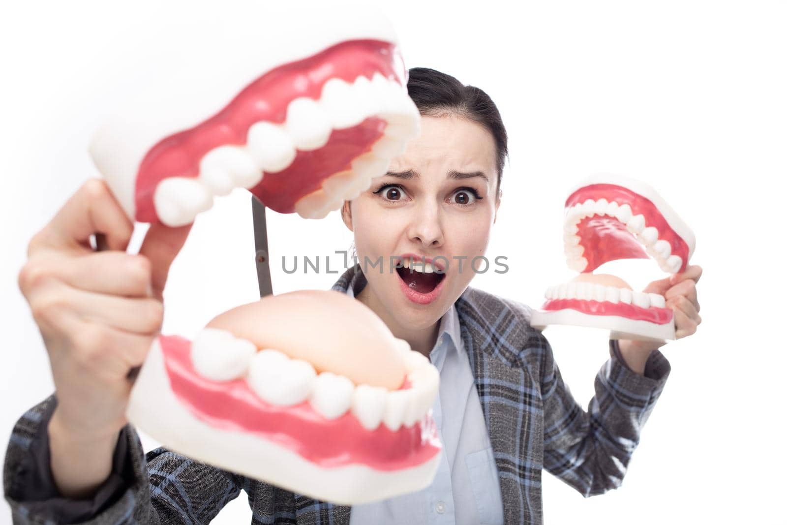 surprised woman in office suit holding dental models of the jaw in her hands, white background by shilovskaya