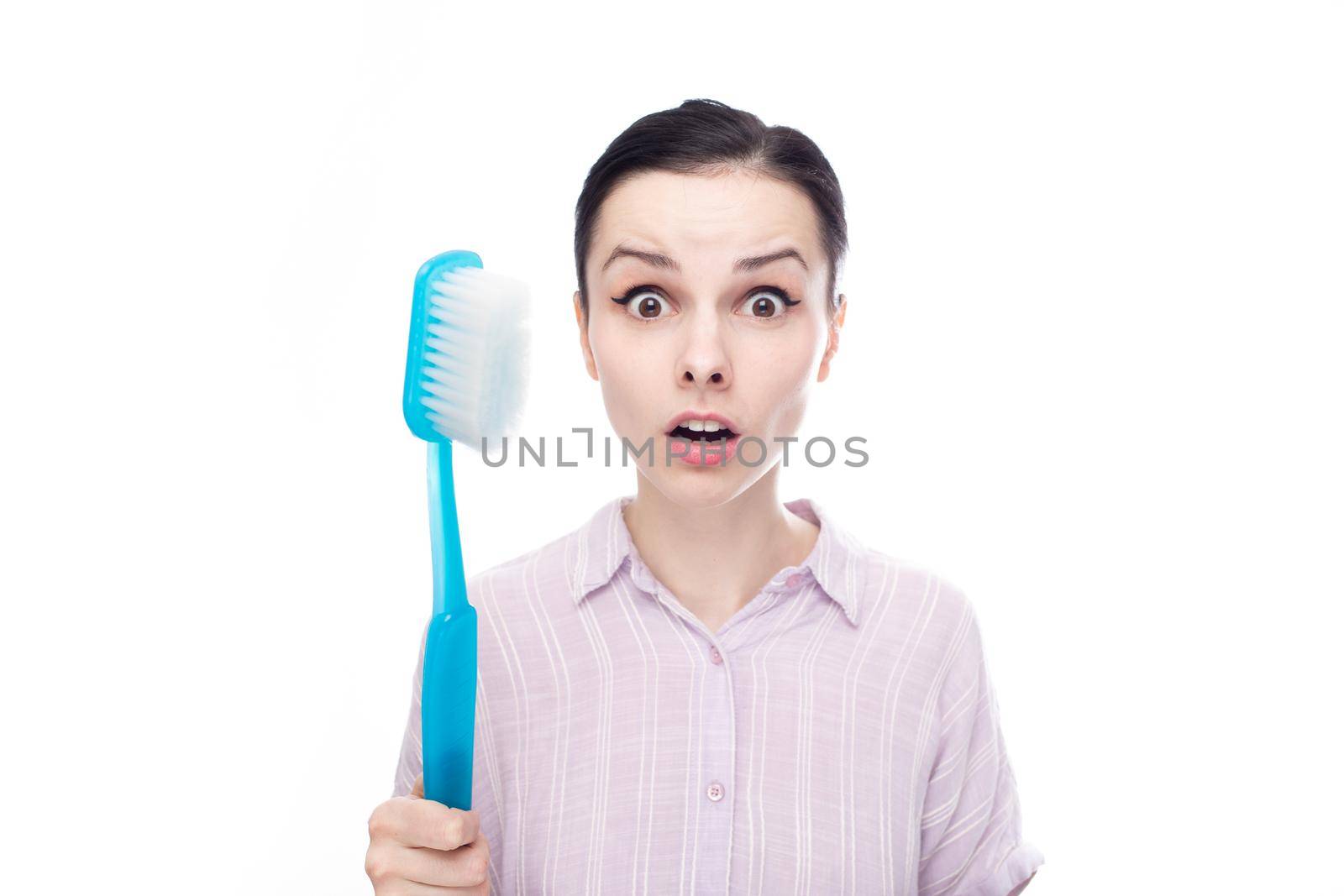 surprised woman in a purple shirt holding a huge blue toothbrush in her hands, white background. High quality photo