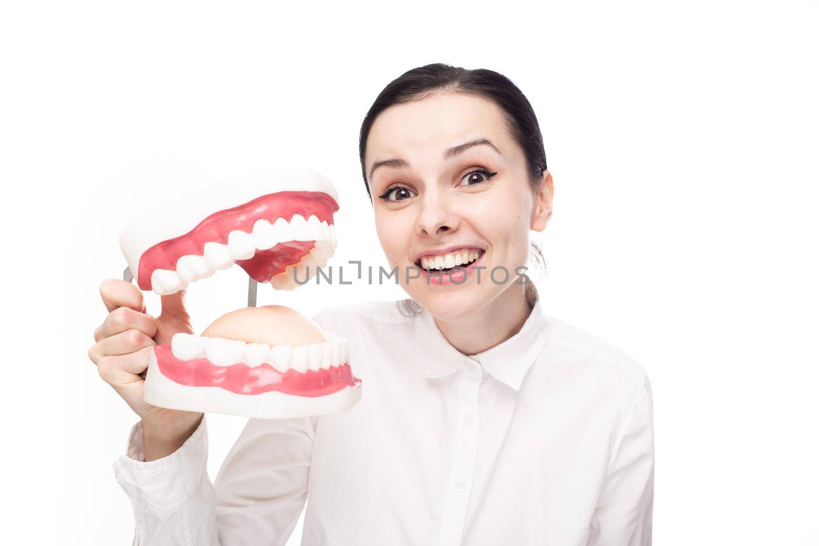 smiling woman dentist in a white shirt holds a large jaw with teeth in her hands, white background by shilovskaya