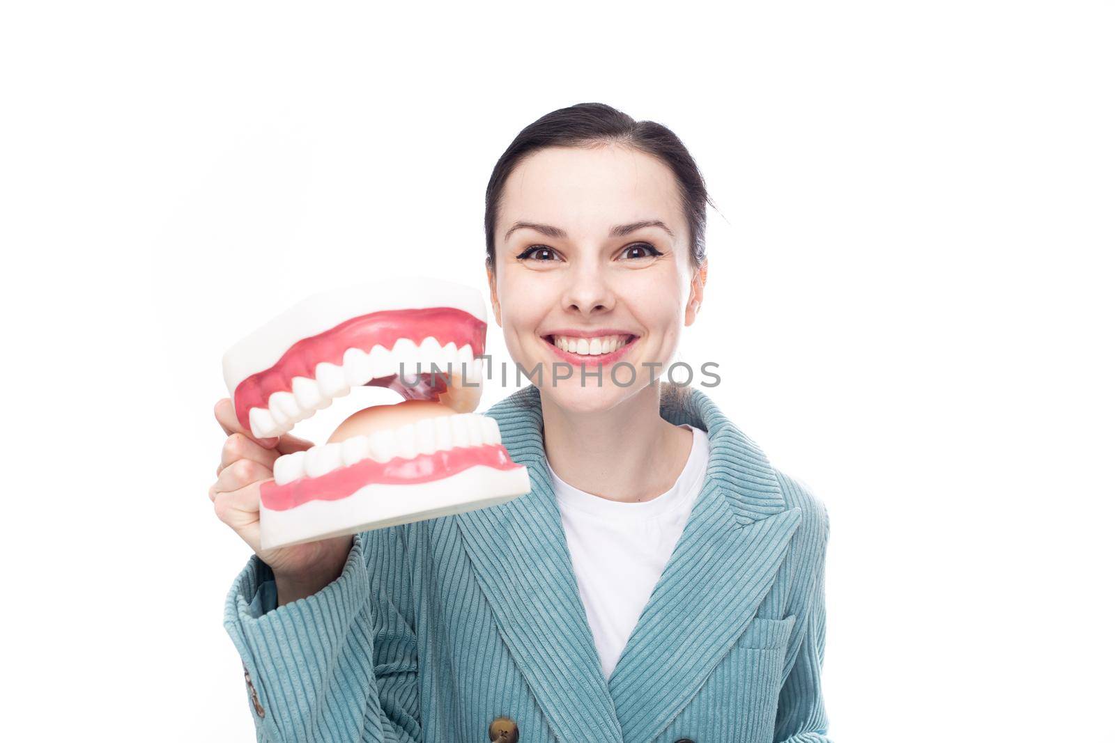 joyful woman in blue velvet jacket holds a huge jaw with teeth in her hand, white background by shilovskaya
