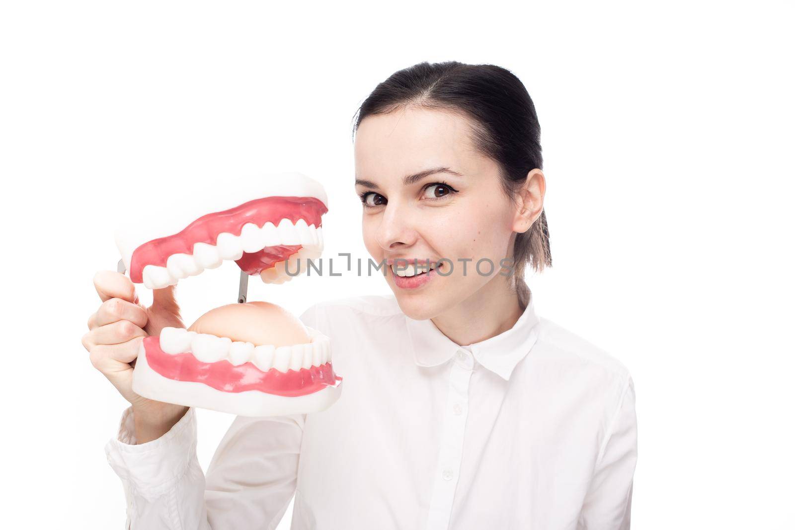 joyful woman dentist in a white shirt holds a large jaw with teeth in her hands, white background by shilovskaya