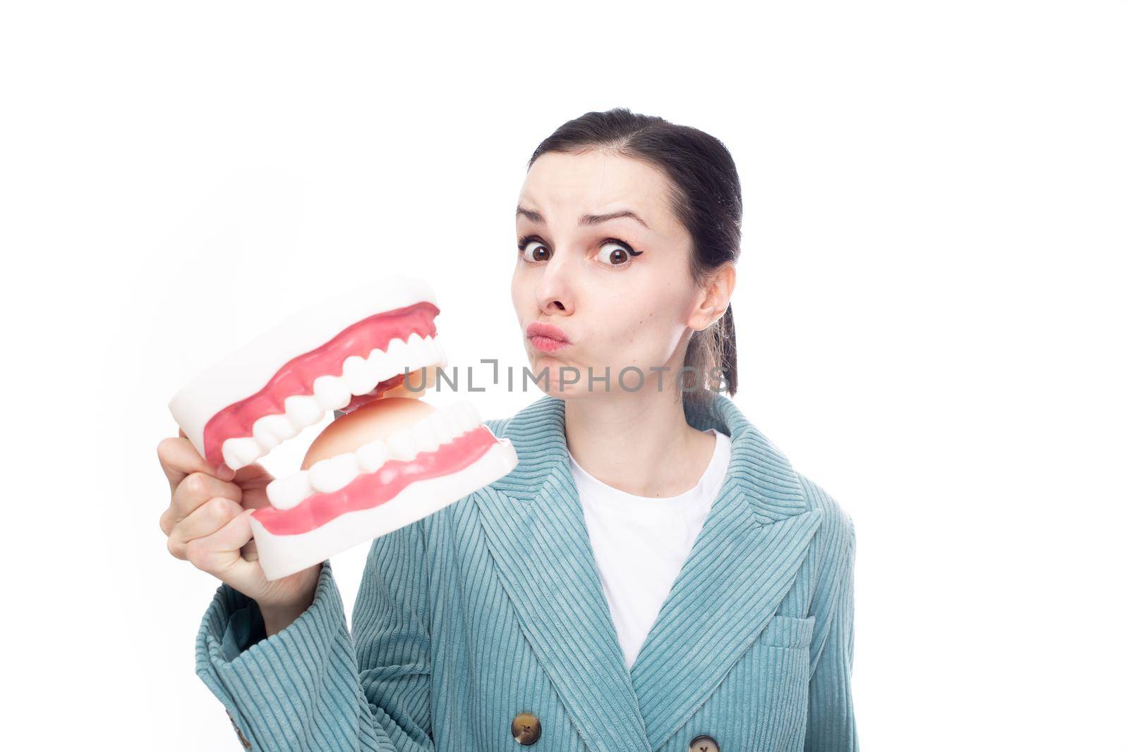 surprised woman in a corduroy jacket holds a huge jaw with teeth in her hand, white studio background. High quality photo