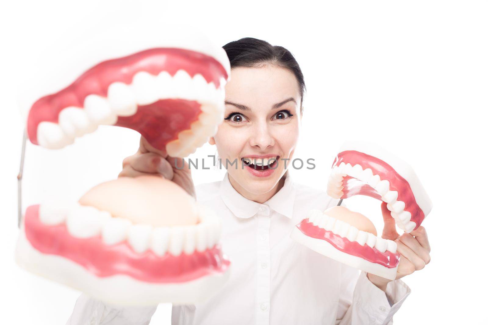 smiling female employee of a dental clinic in a white shirt holding giant jaws in her hands. High quality photo