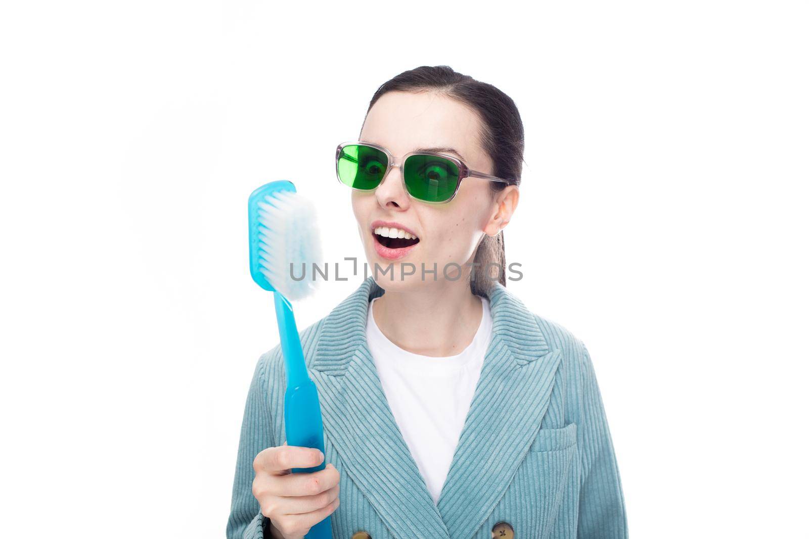 funny woman in green glasses holds a big toothbrush in her hand, white background. High quality photo