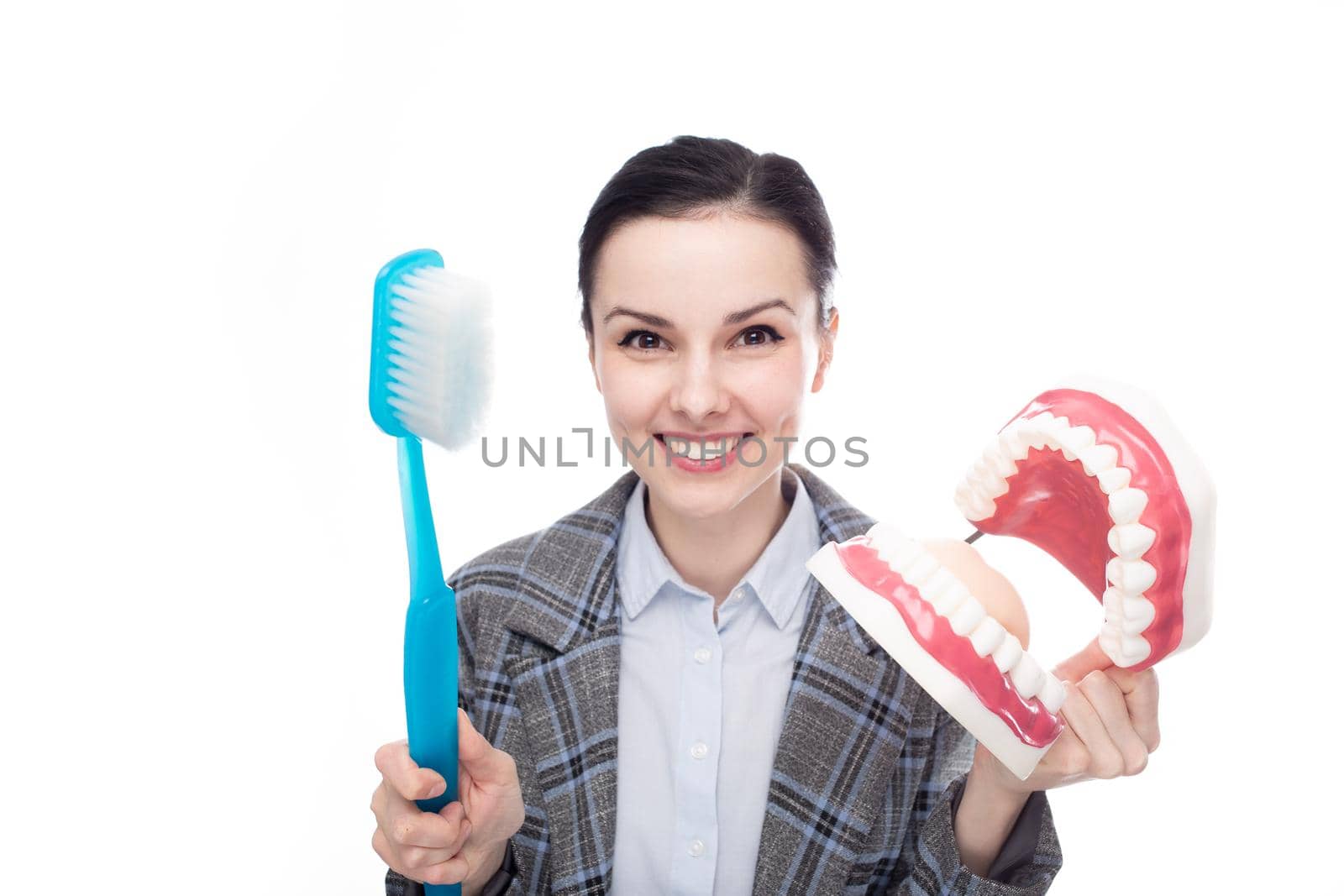 happy woman in office suit holding big toothbrush and big jaw mockup with teeth, white background. High quality photo