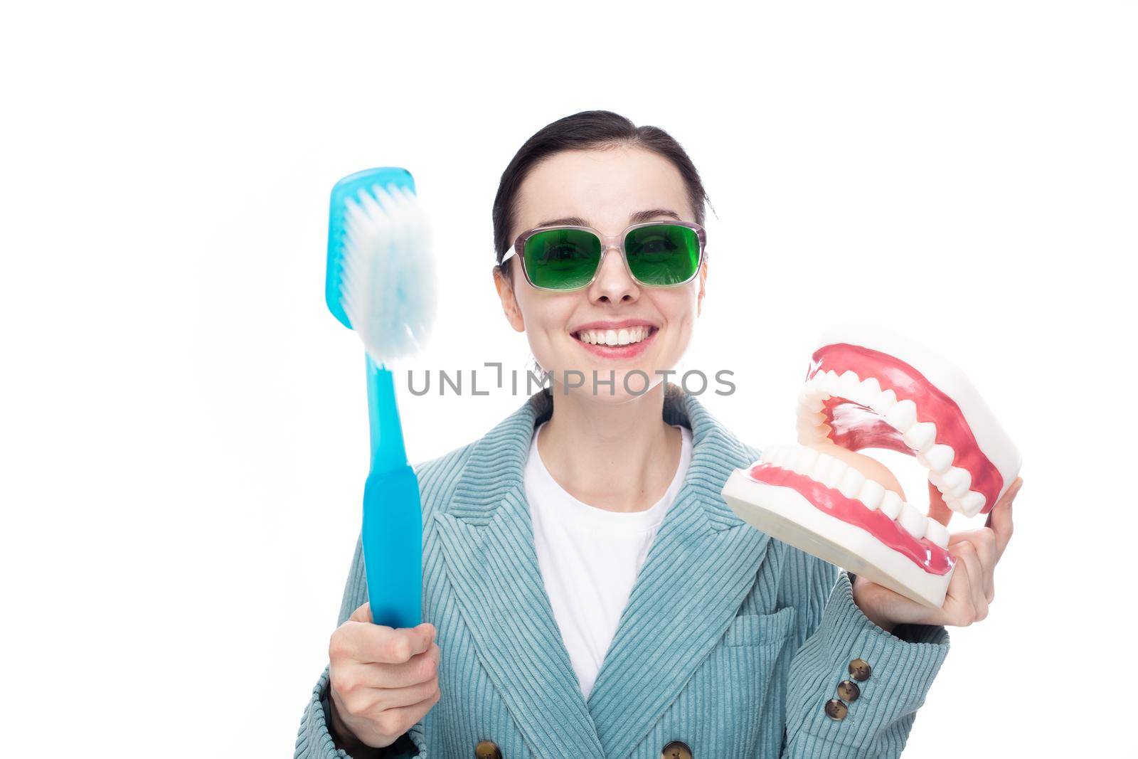 funny woman in green glasses holding big toothbrush and big jaw mockup, white background. High quality photo