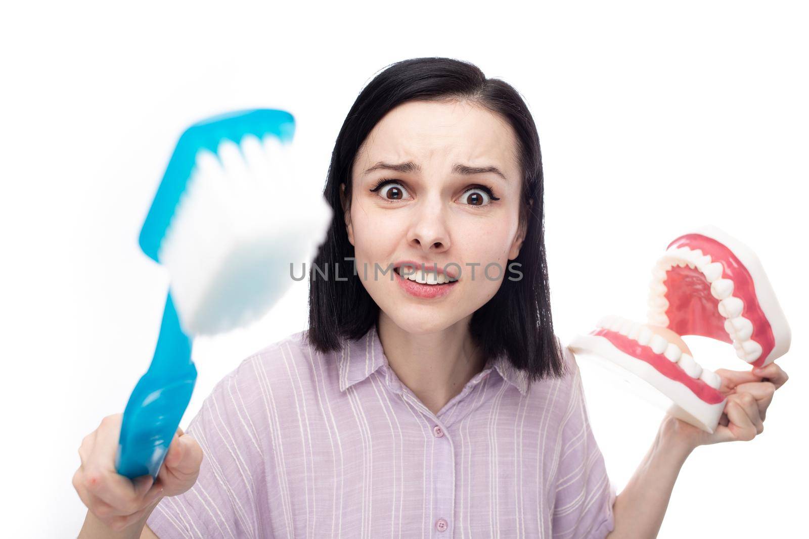 surprised woman in a purple shirt holding a huge toothbrush in her hand a huge jaw mockup by shilovskaya