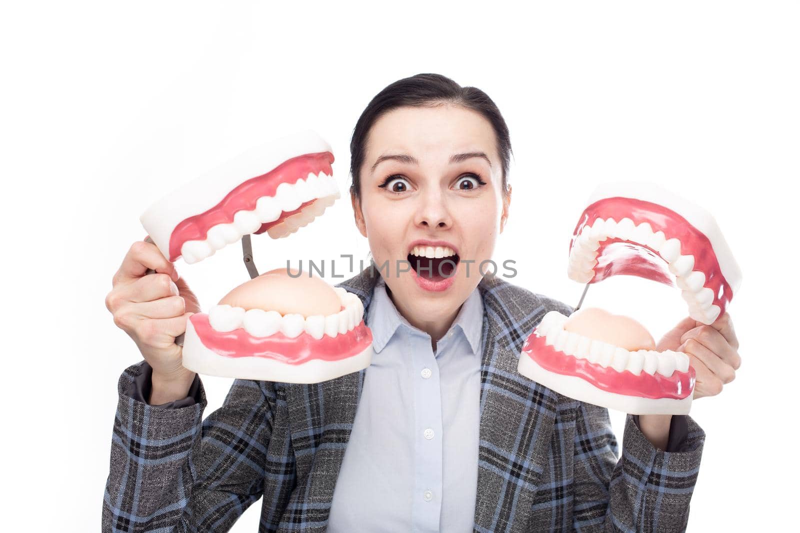 surprised woman in office suit holding dental models of the jaw in her hands, white background by shilovskaya