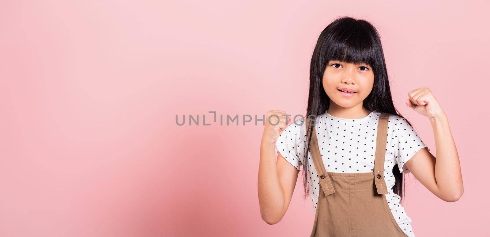 Yes ! Asian little kid 10 years old celebrating great success with arms raised at studio shot isolated on pink background, Happy and excited child girl positive smiling cheerful