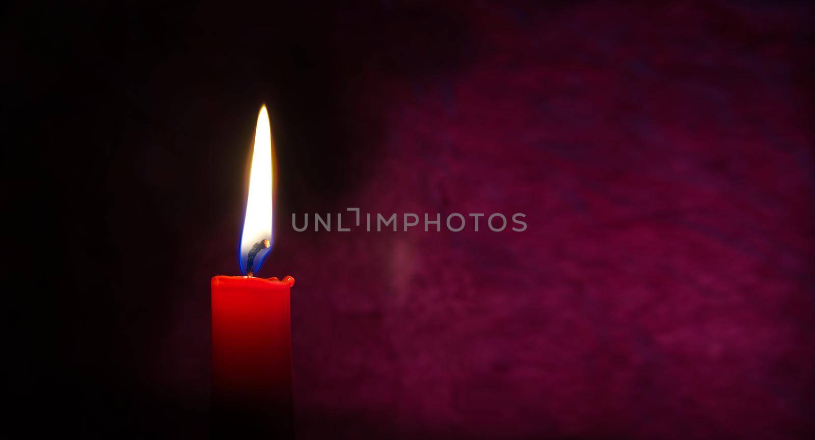 Single red candle burning alone in the dark red background. Conceptual image of peace, love, hope or patience in a panorama banner with free copy space