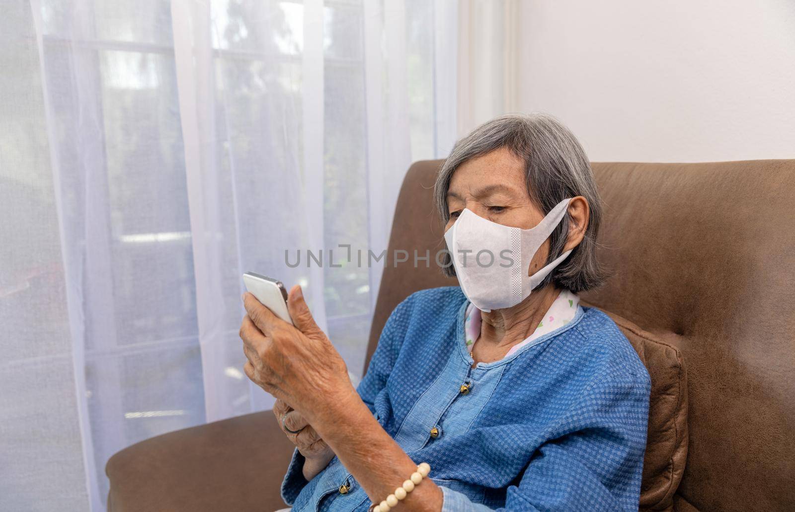 Covid-19 pandemic, Elderly asian woman relax on couch in living room browsing wireless Internet on cellphone.