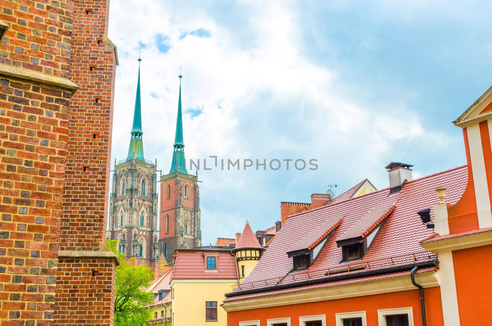 View of two towers with spires of Cathedral of St. John the Baptist catholic church and tiled roofs of buildings with blue cloudy sky in old historical city centre, Ostrow Tumski, Wroclaw, Poland