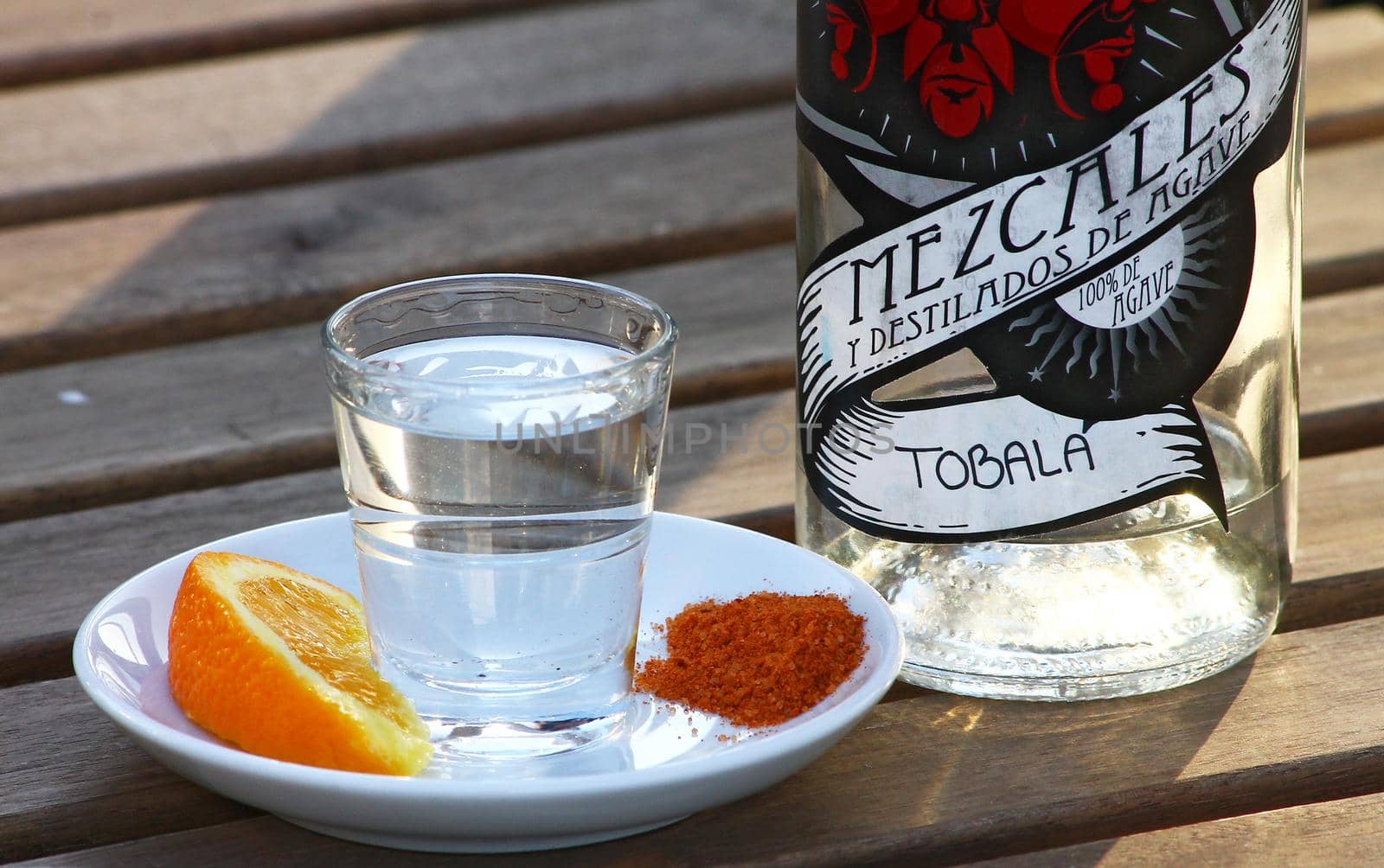 Mexcal bottle and small glass, with orange slice and gusano salt on a wooden table