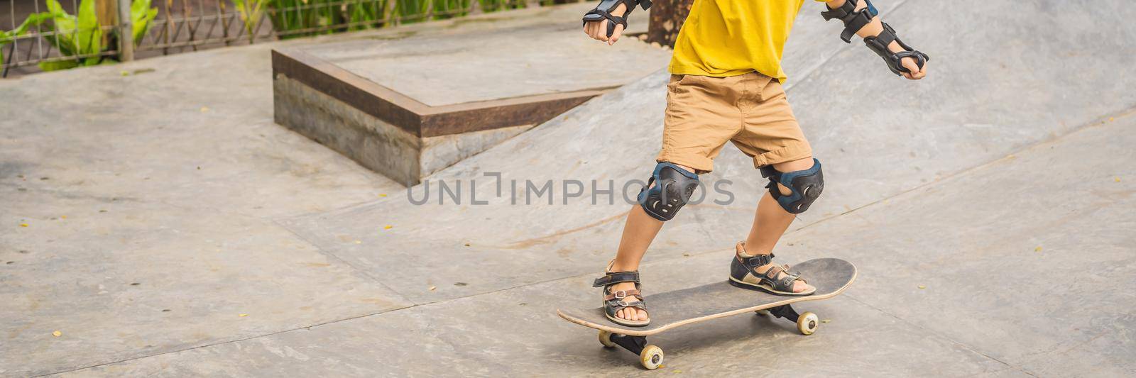 Athletic boy in helmet and knee pads learns to skateboard with in a skate park. Children education, sports BANNER, LONG FORMAT by galitskaya