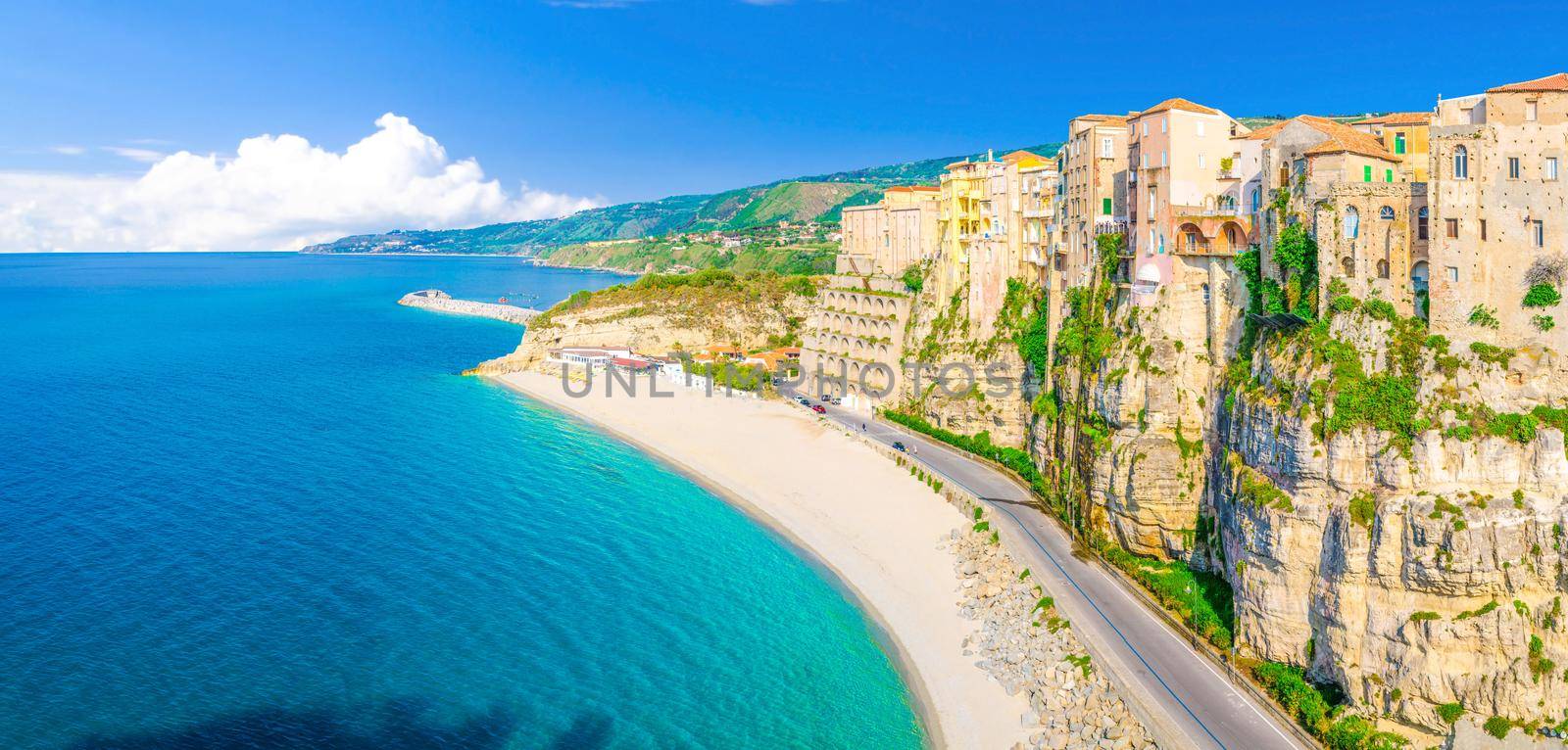 Aerial panoramic view of Tropea town and beach coastline of Tyrrhenian Sea with turquoise azure water, colorful houses buildings on top of high big rocks, road along sea, Calabria, Southern Italy