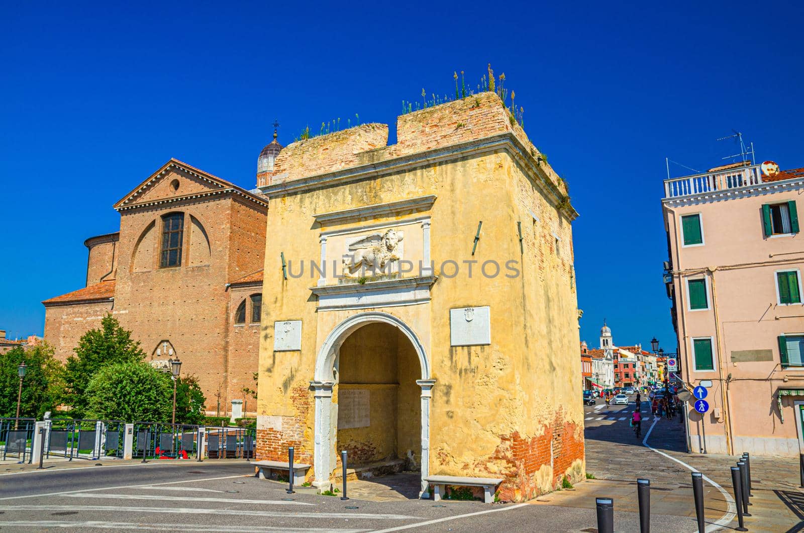 Porta Santa Maria o Porta Garibaldi gate and Cathedral Santa Maria Assunta Duomo catholic church in Chioggia town historical centre, blue sky background in summer day, Veneto Region, Northern Italy