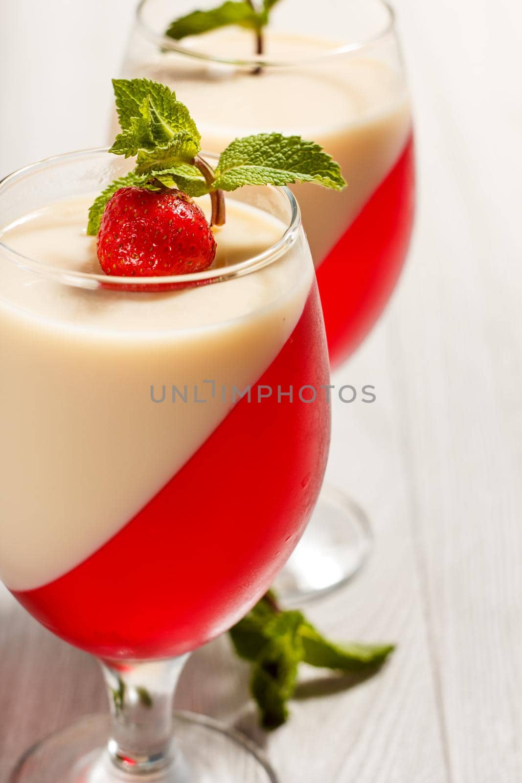 Cherry and milk jelly in the glasses decorated with mint leaves and strawberry on the wooden background