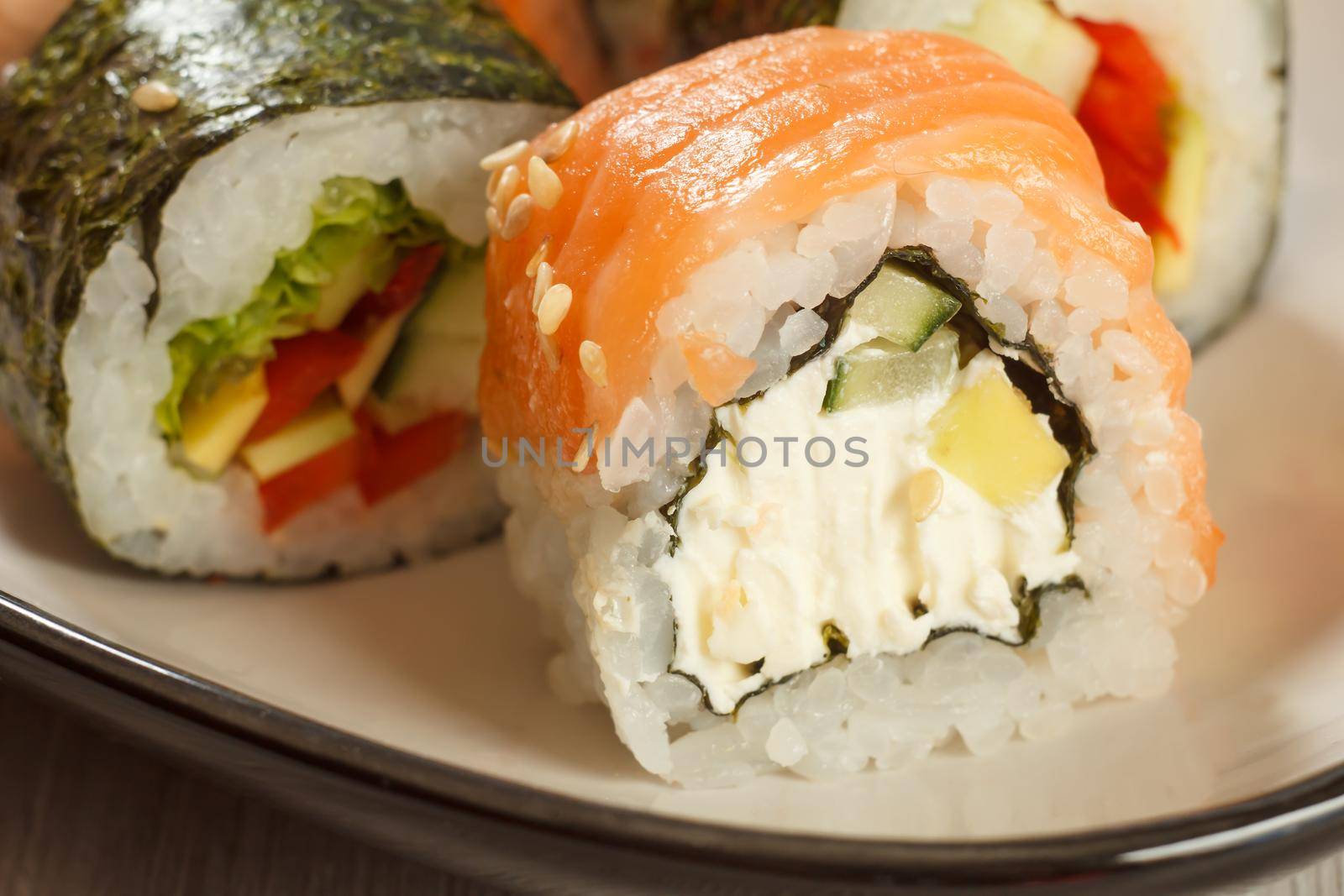 Close up Uramaki Philadelphia. Sushi rolls with salmon, nori, rice, Philadelphia cheese, pieces of avocado, cucumber and sushi rolls with vegetables on the background. Japanese cuisine. Shallow depth of field