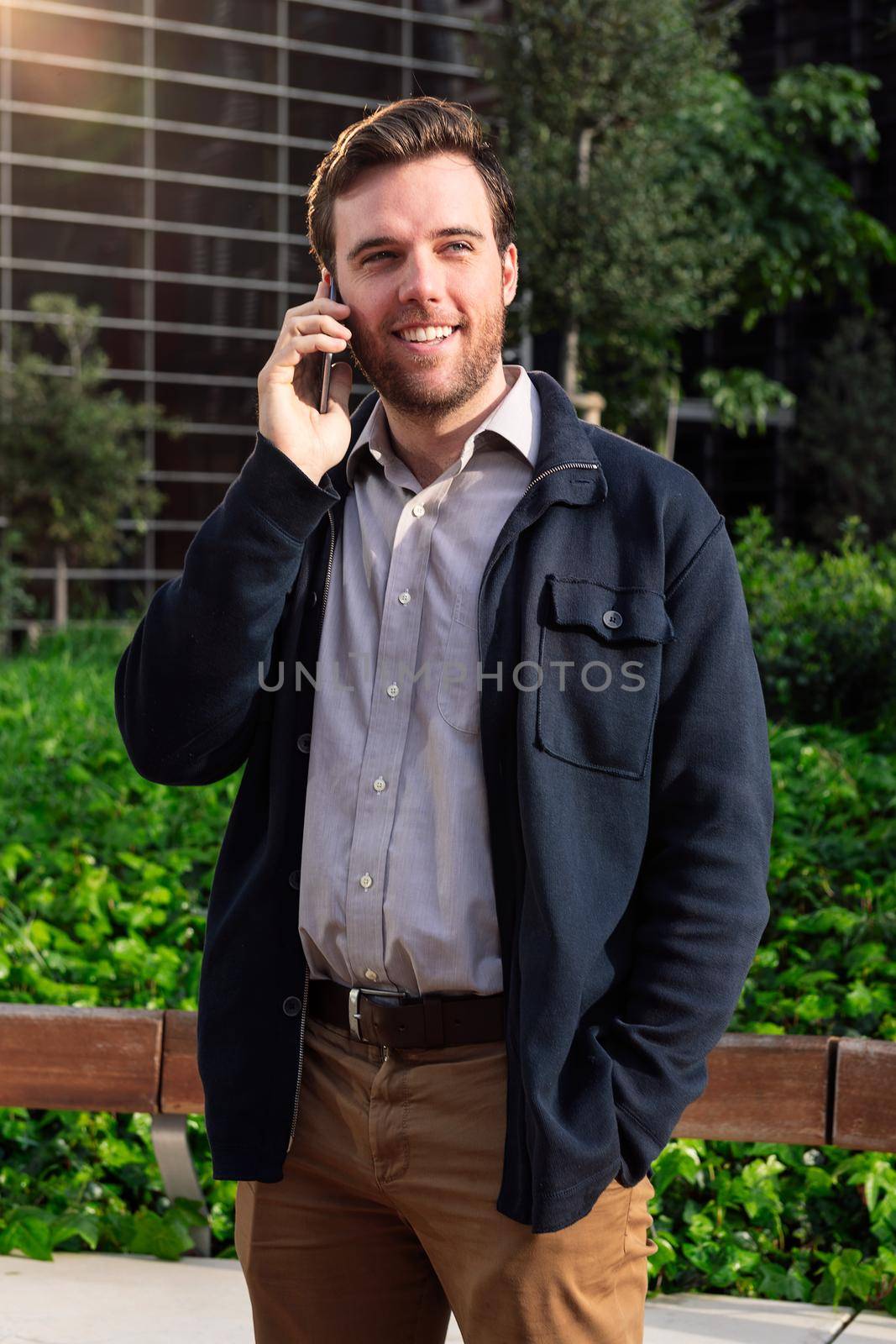 caucasian business man talking on the phone in a park next to an office building, concept of technology and communication