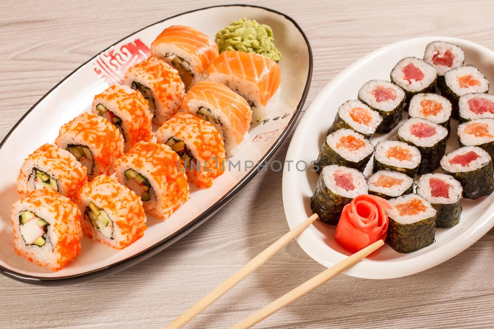 Different sushi rolls with rice, vegetable, seafood on ceramic plates on wooden desk. Top view