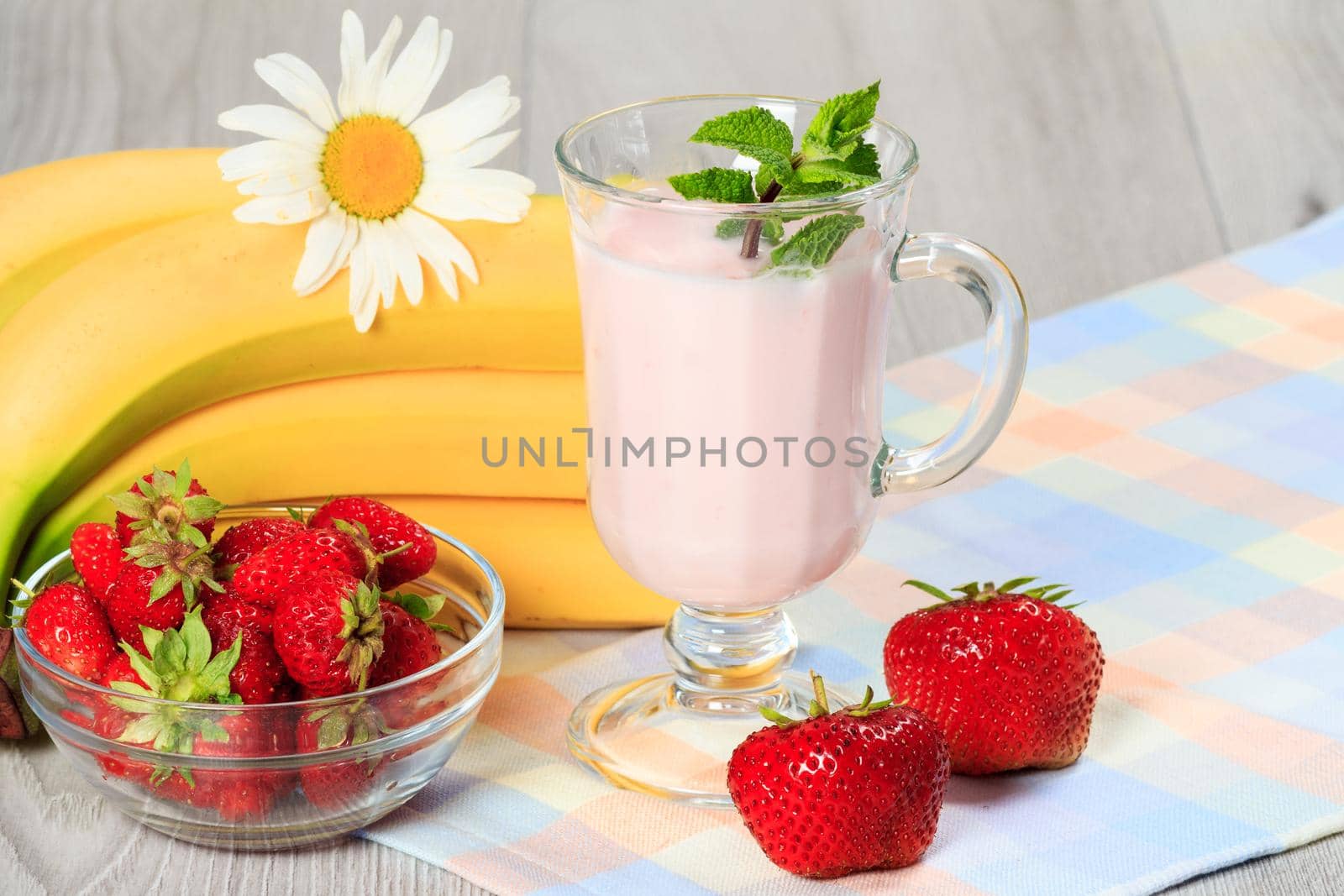 Glass of delicious yogurt with mint and fresh strawberries, banana, chamomile on a wooden table with a napkin