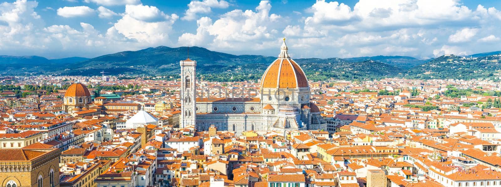 Top aerial panoramic view of Florence city with Duomo Cattedrale di Santa Maria del Fiore cathedral, buildings houses with orange red tiled roofs and hills range, blue sky white clouds, Tuscany, Italy