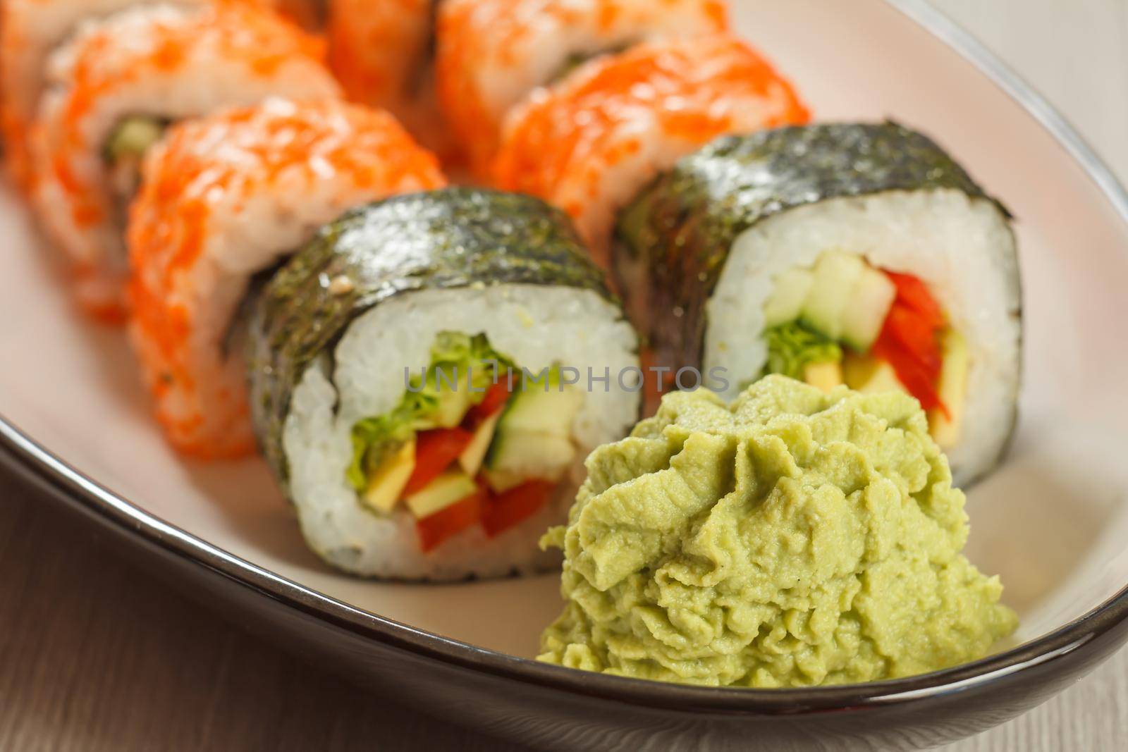 Close up wasabi and sushi rolls with vegetables, Uramaki California on the background. Japanese cuisine. Shallow depth of field. Focus on wasabi