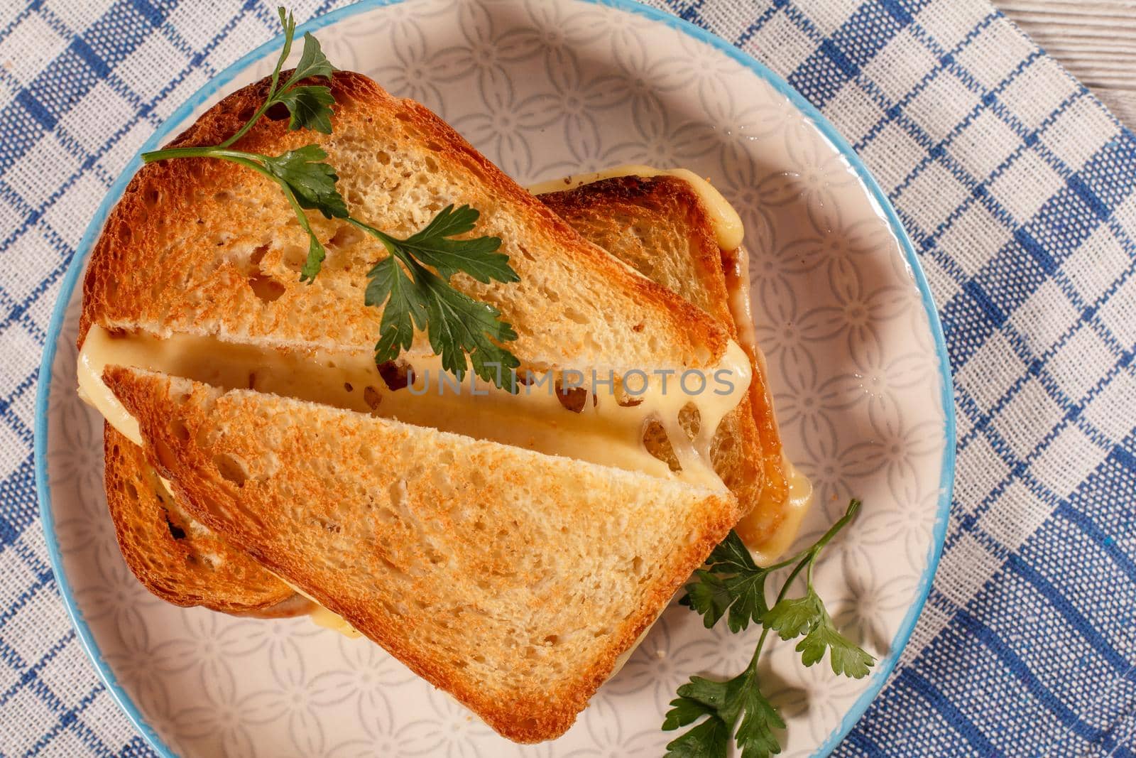 Toasted slices of bread with cheese and green parsley on white plate with blue kitchen napkin. Good food for breakfast. Top view