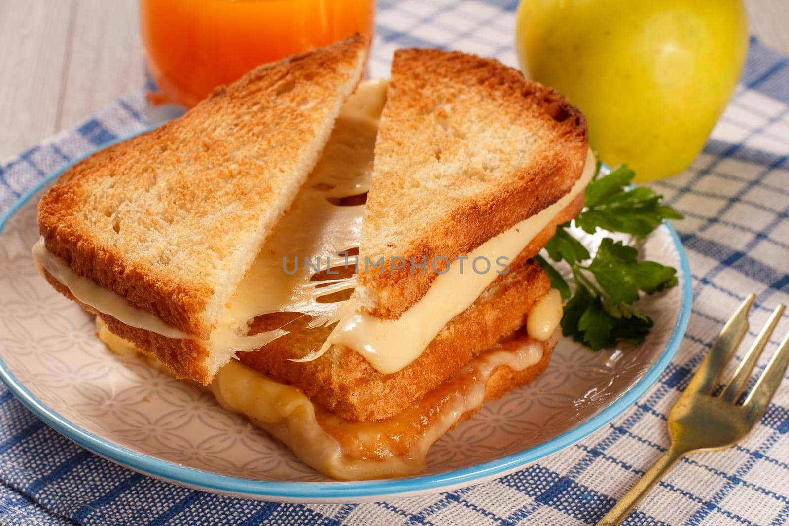 Toasted slices of bread with cheese and green parsley on white plate, glass of orange juice and green apple with blue kitchen napkin. Good food for breakfast