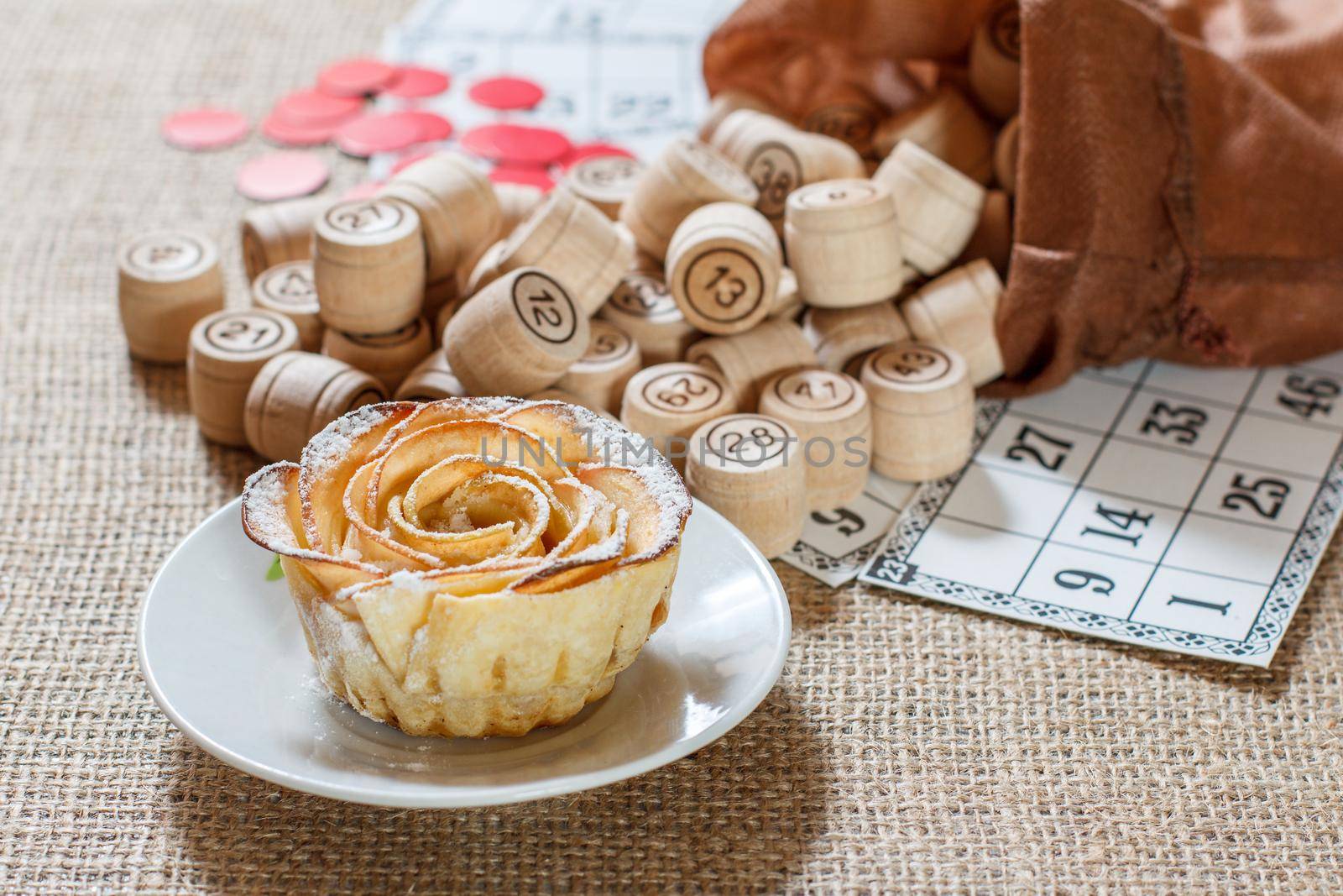 Wooden lotto barrels in brown pouch and game cards for a game in lotto with homemade biscuit in the form of rose on white saucer