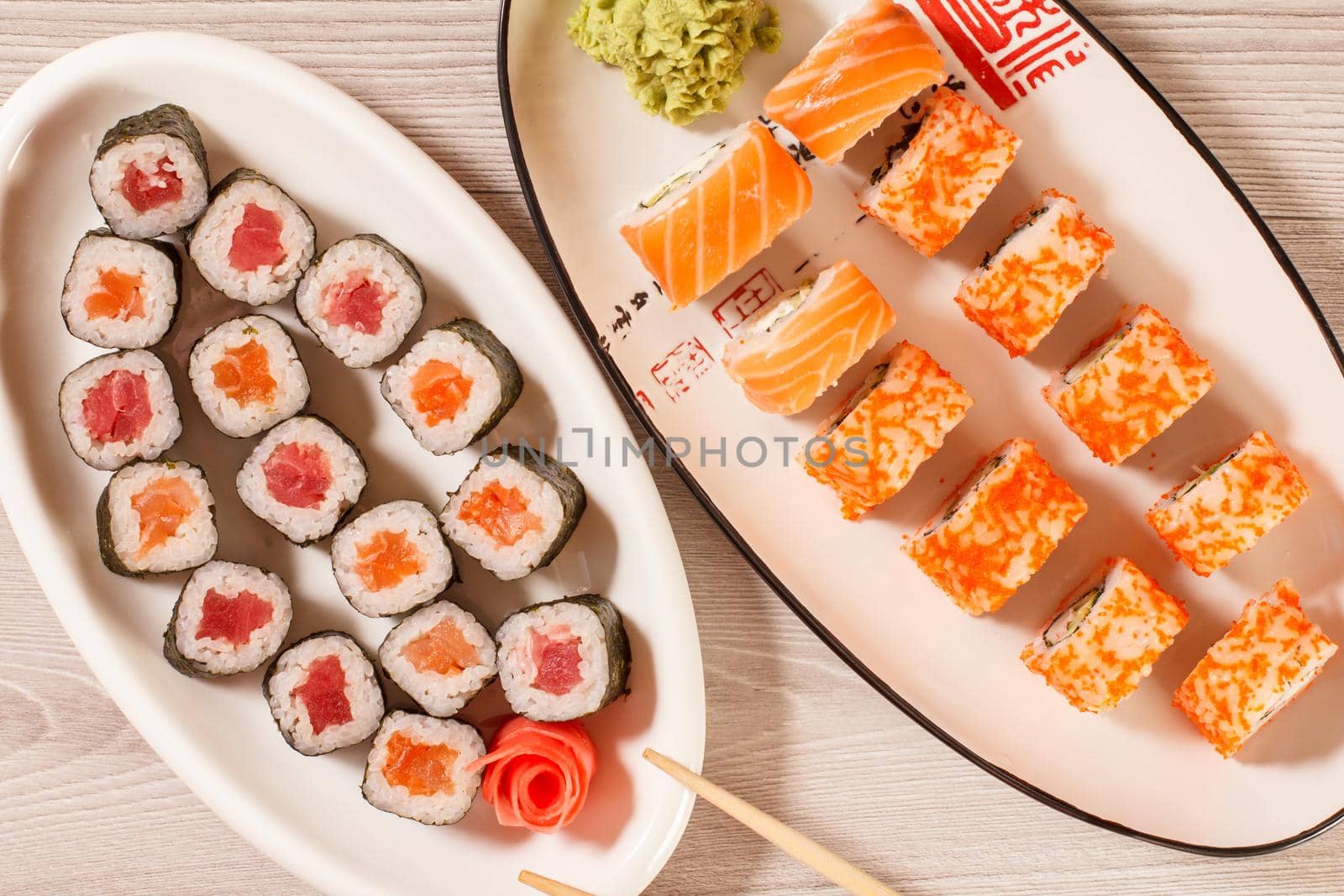 Different sushi rolls with rice, vegetable, seafood on ceramic plates on wooden desk. Top view