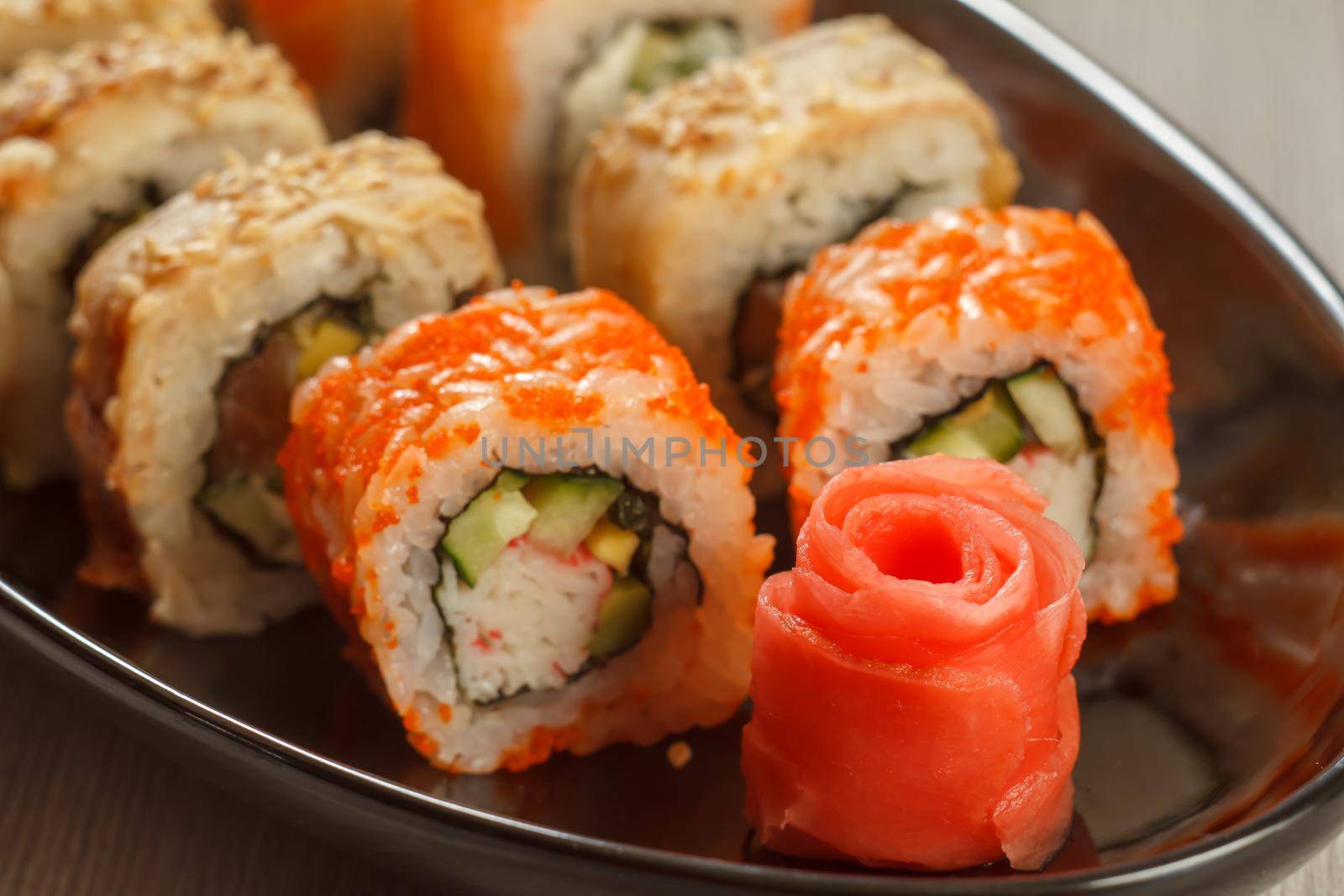 Close up pickled ginger in the form of red rose and sushi rolls - Uramaki California, Uramaki with Conger on the background. Japanese cuisine. Shallow depth of field. Focus on ginger