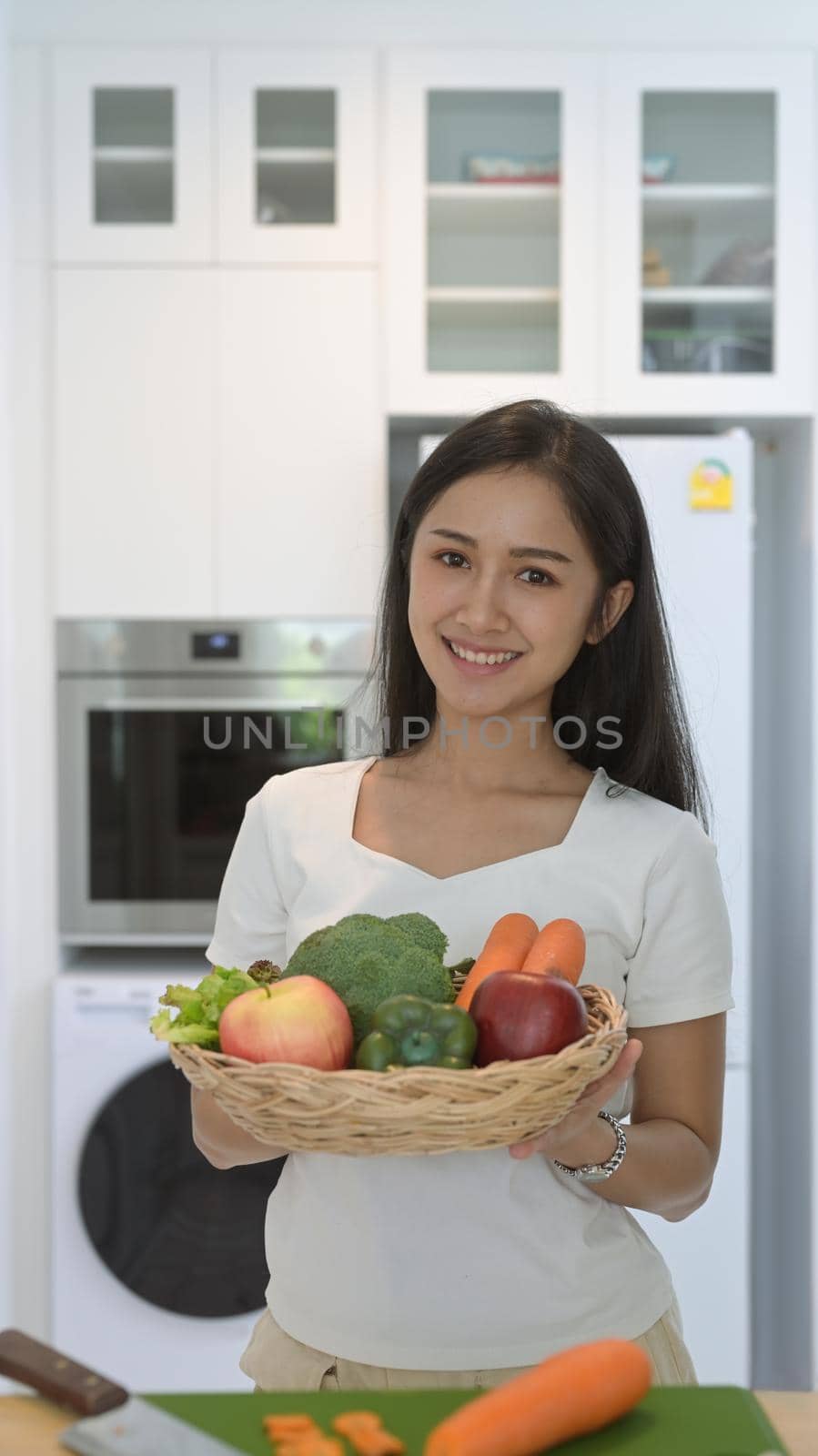 Portrait asian woman holding wicker basket with fresh organic vegetables and fruits standing in home office.