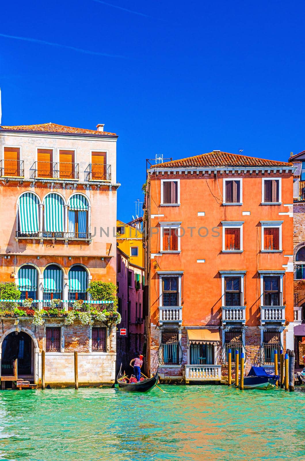 Grand Canal waterway in Venice historical city centre with gondolier on sailing gondola and Venetian architecture colorful buildings, blue sky in sunny day background. Veneto Region, Northern Italy.