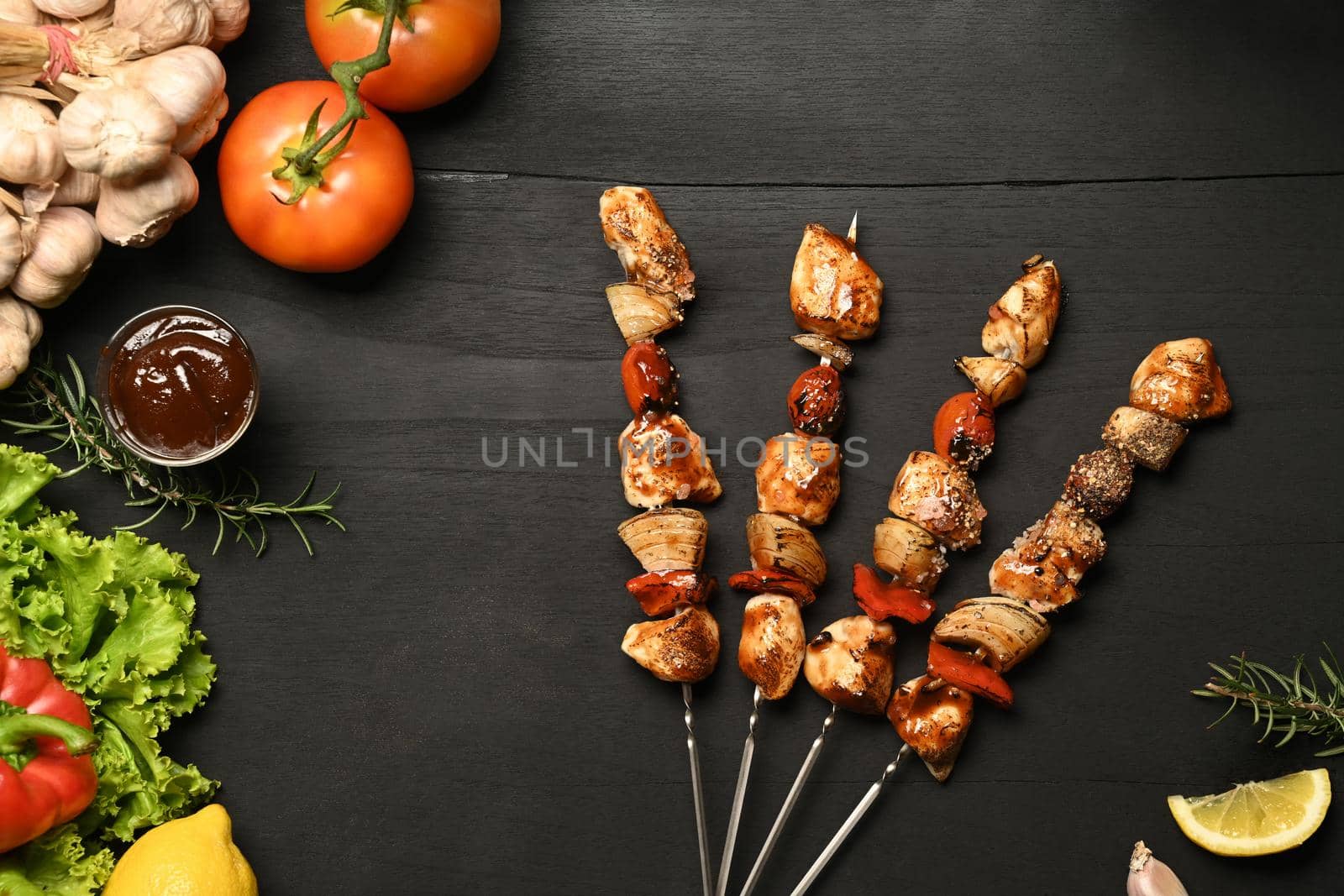 Tasty barbecue skewers with grilled chicken, cherry tomato, sweet pepper, onions and barbecue sauce on dark stone background.
