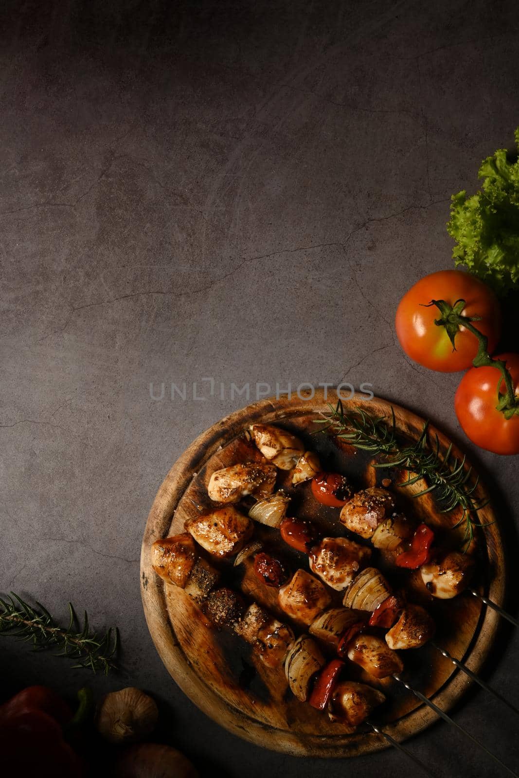 Delicious grilled skewers of chicken, bell peppers, tomatoes, onion and barbecue sauce on dark stone background.