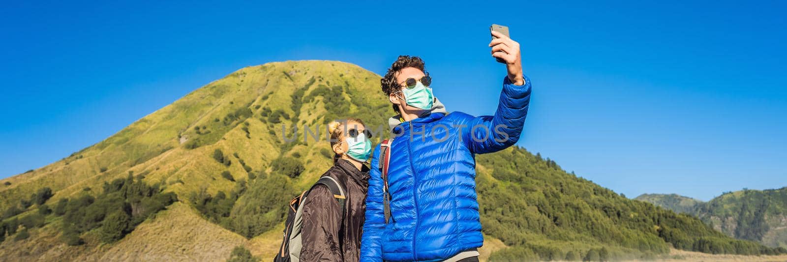 BANNER, LONG FORMAT Young man and woman tourists make a selfie in the Bromo Tengger Semeru National Park on the Java Island, Indonesia. They enjoy magnificent view on the Bromo or Gunung Bromo on Indonesian, Semeru and other volcanoes located inside of the Sea of Sand within the Tengger Caldera. One of the most famous volcanic objects in the world. Travel to Indonesia concept by galitskaya