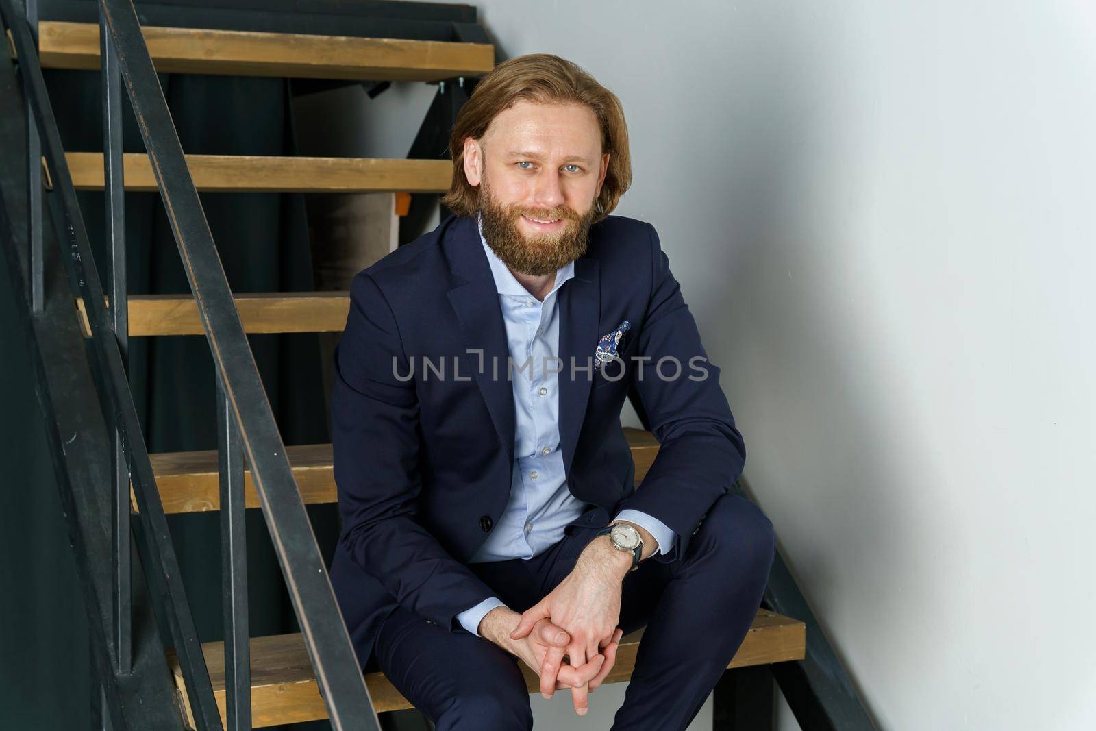 a handsome brutal bearded and long-haired man sits on the steps of the stairs, a stylish businessman. High quality photo