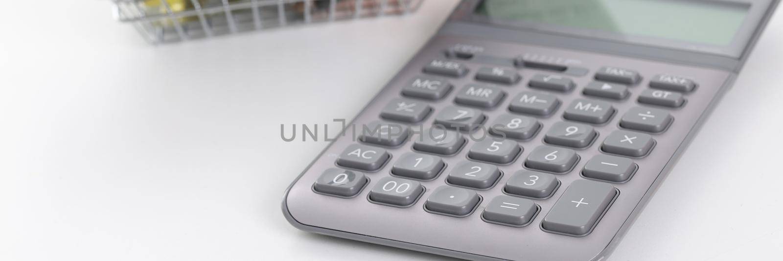 Calculator and basket with pills and capsules on a white background, close-up. Expenses for food supplements and vitamins, drug revenue