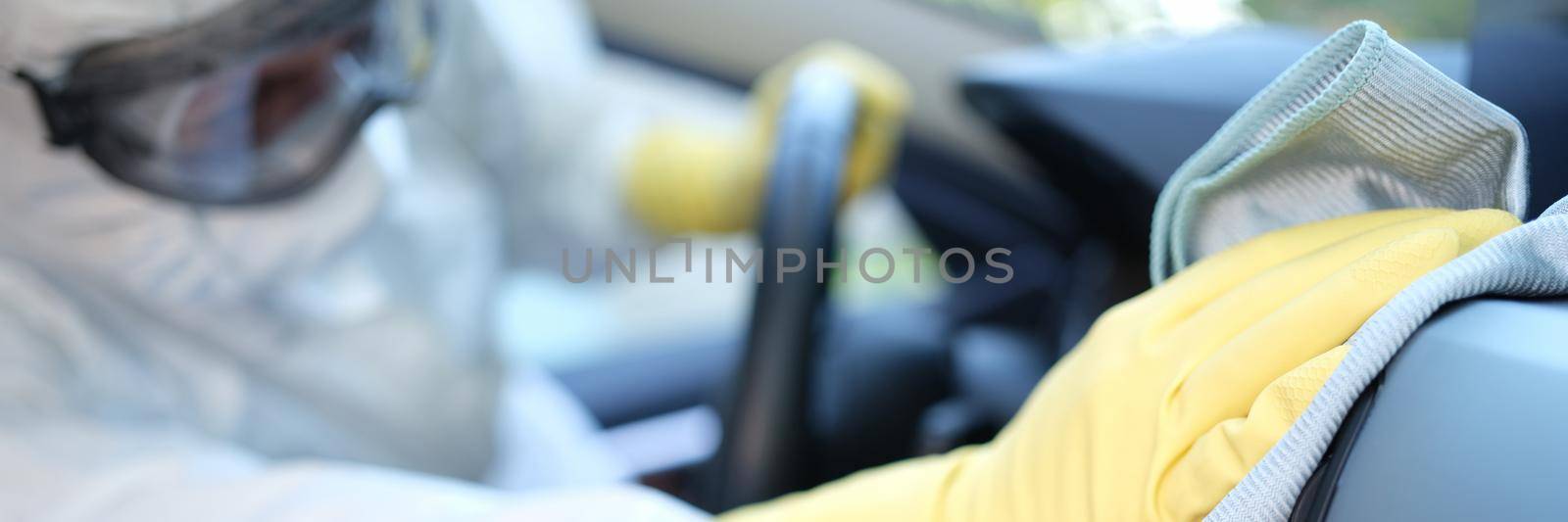 A man in a uniform wipes the interior of a car with a towel, close-up. Professional dry cleaning in a car service