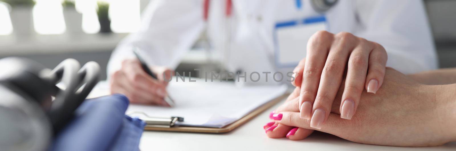 A woman doctor in a clinic holds the patient's hand, close-up. Family doctor's appointment, disease diagnosis, patient appointment