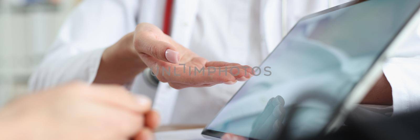 A woman doctor shows a tablet to a patient, close-up of a hand. Consultation in the clinic, diagnostics of patient analyzes