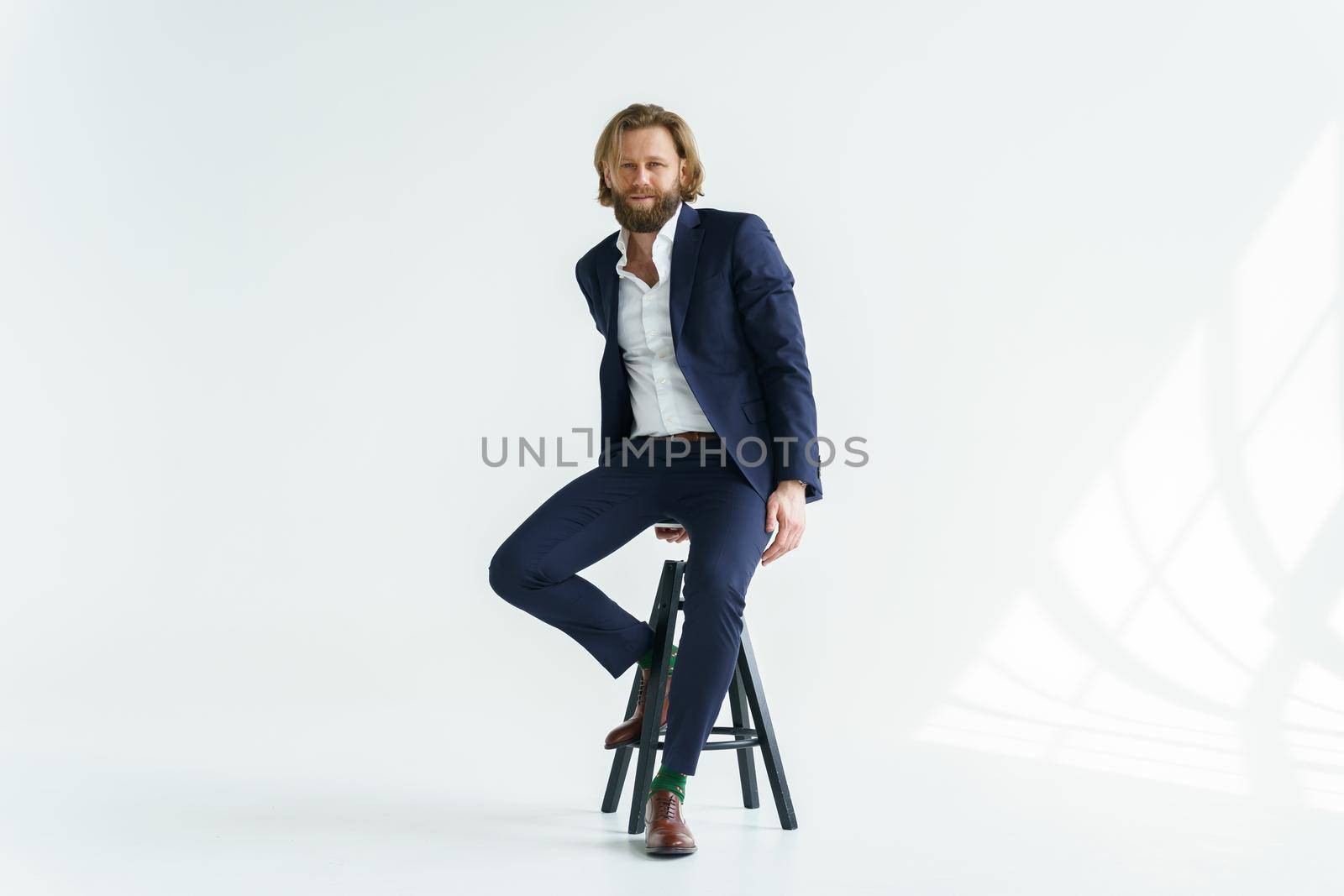 a handsome brutal bearded and long-haired man, a stylish businessman sitting on a chair with a white background. High quality photo