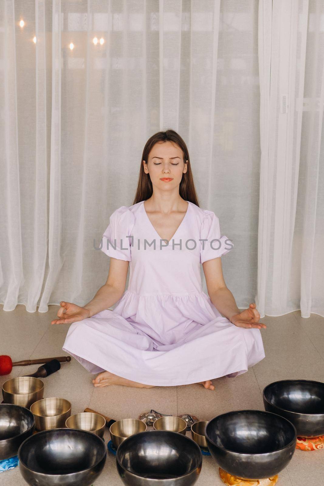 A woman sits with Tibetan bowls in the lotus position before doing yoga in the gym.