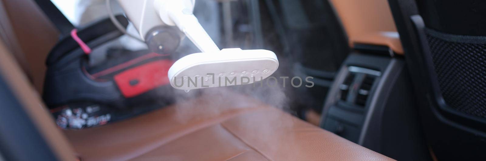 A man in protective clothing cleans the interior of a car from dirt, close-up. Professional household appliances, steam vacuum cleaner