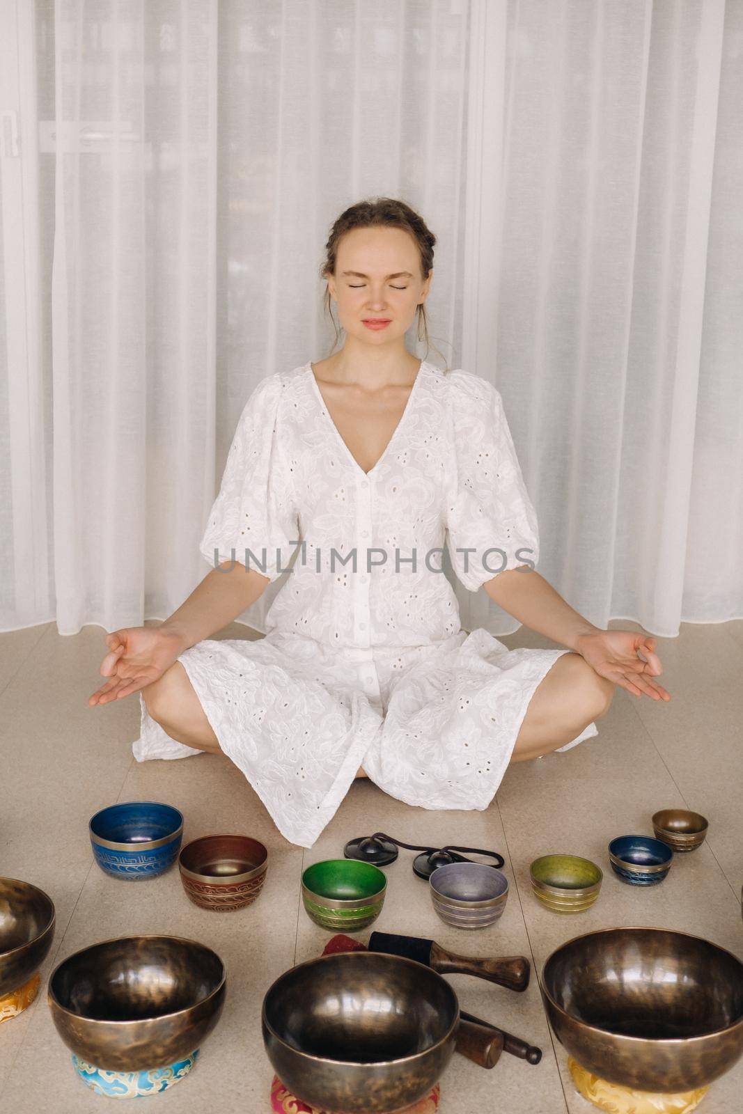 A woman sits with Tibetan bowls in the lotus position before doing yoga in the gym.