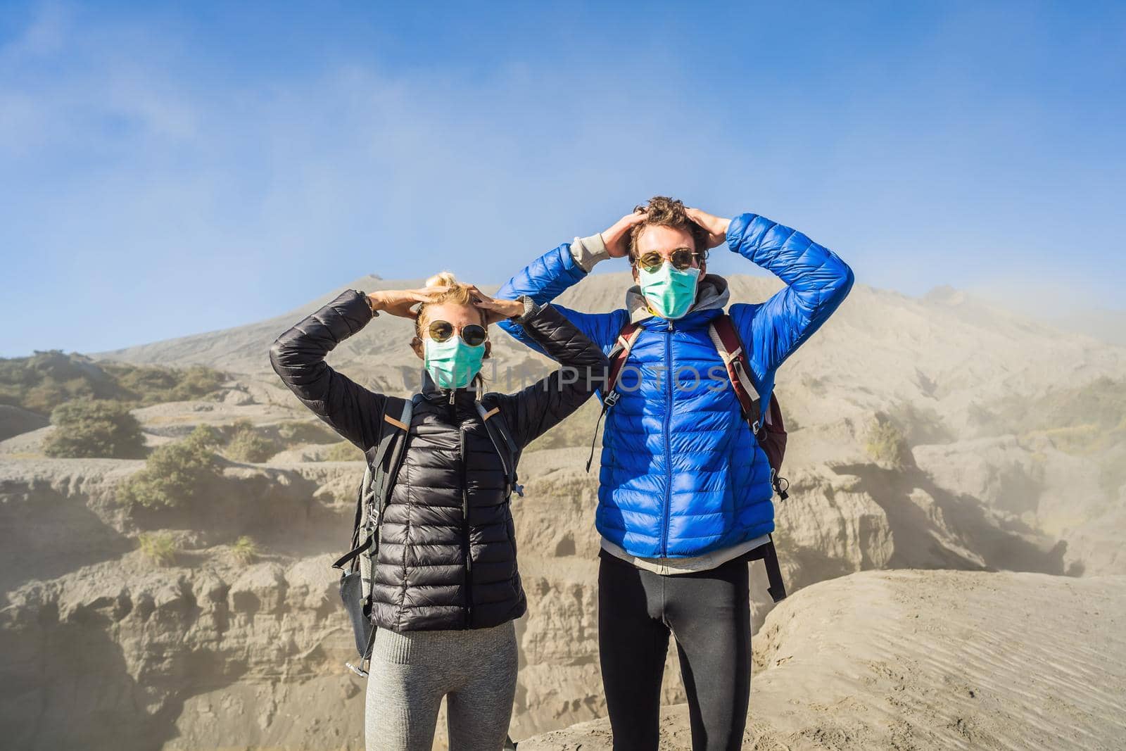 Young couple man and woman visit the Bromo volcano at the Tengger Semeru National Park on Java Island, Indonesia. They are scared of the eruption covering everything with dust and they wear safety masks to protect themselves from dangerous volcanic ash. Concept of tourists in trouble caused by a volcano.