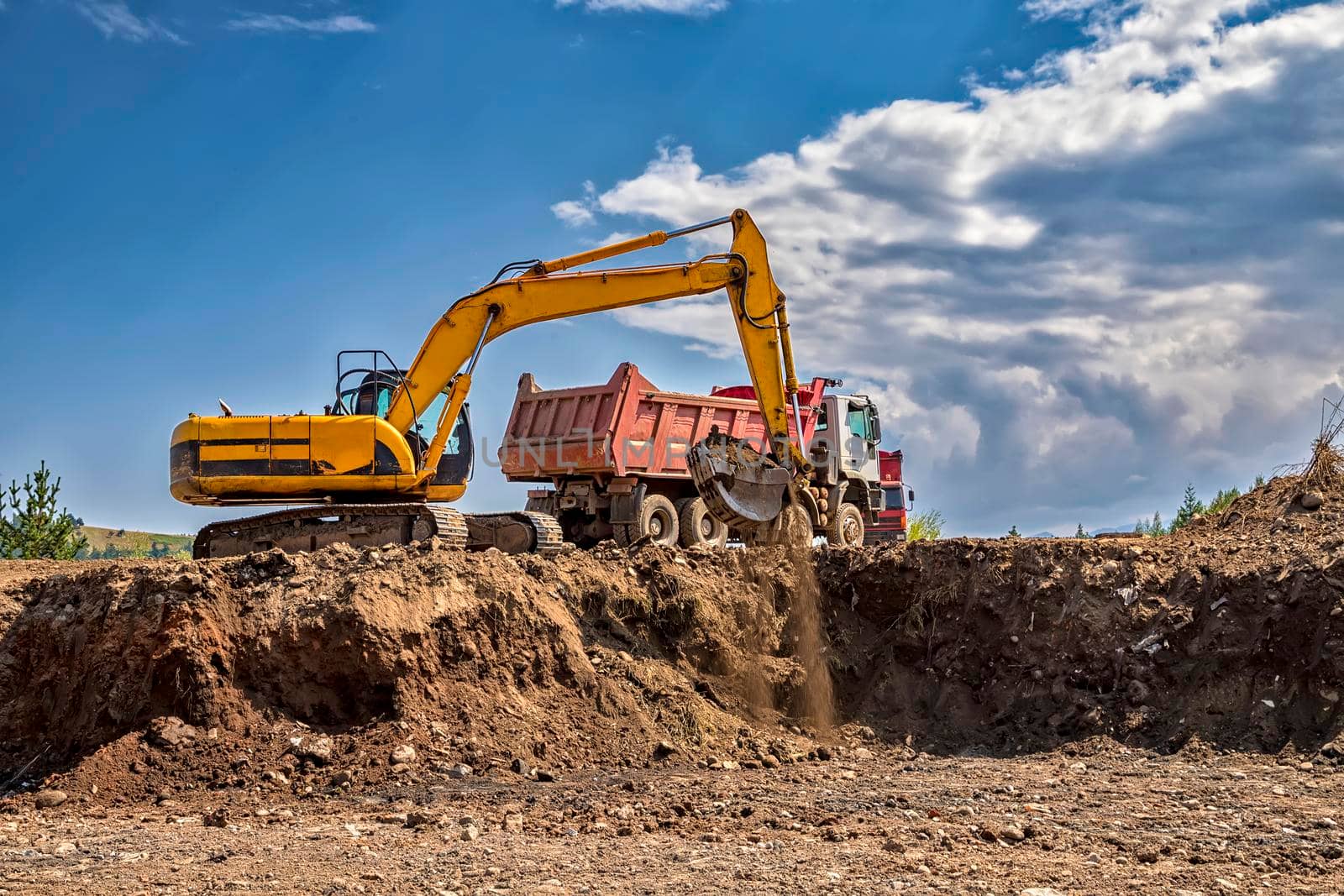 Yellow excavator and empty truck working at the construction site