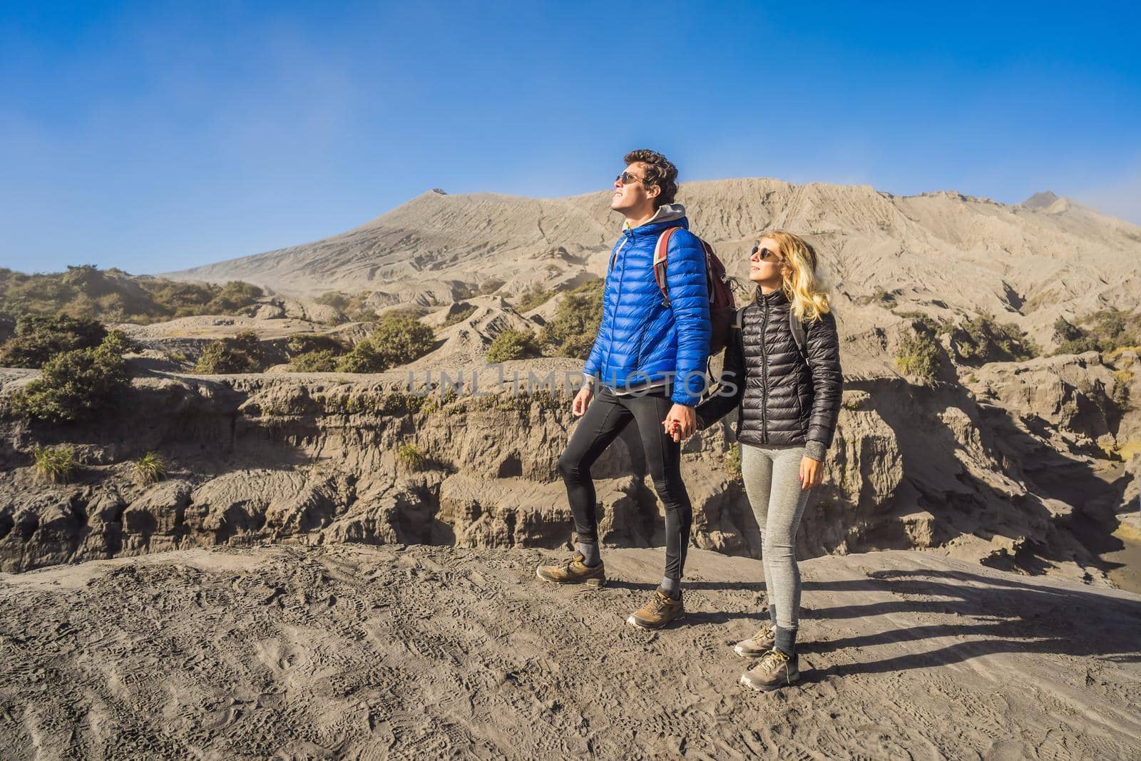 Young couple man and woman visit the Bromo volcano at the Tengger Semeru National Park on the Java Island, Indonesia. They enjoy magnificent view on the Bromo or Gunung Bromo on Indonesian, Semeru and other volcanoes located inside of the Sea of Sand within the Tengger Caldera. One of the most famous volcanic objects in the world. Travel to Indonesia concept.