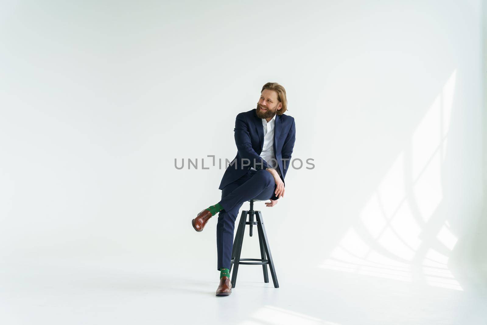 a handsome brutal bearded and long-haired man, a stylish businessman sitting on a chair with a white background. High quality photo